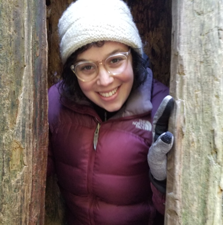Photo of staff member Lilly Schneider smiling from inside a hollow tree.