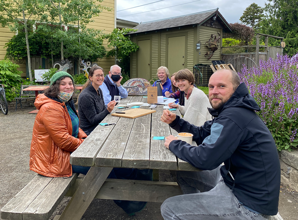 Six people sit at a picnic table in a courtyard.