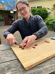 A smiling woman cuts chocolate squares on a cutting board.