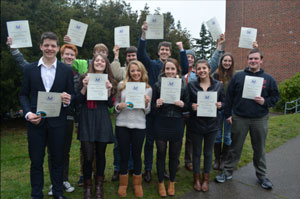 A group of smiling teenagers waving award certificates.