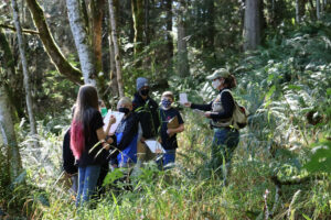 Group of students and an adult huddled in a forest.