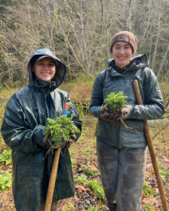 Two girls in raincoats holding weeds and shovels.