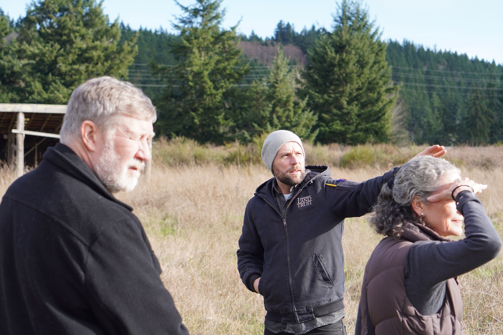 Lg4WebDSC06685-Chimacum-Commons-Visit-credit-Olympic-Housing-Trust On a site visit at the Chimacum Commons property, three people in a field with evergreen forest behind them