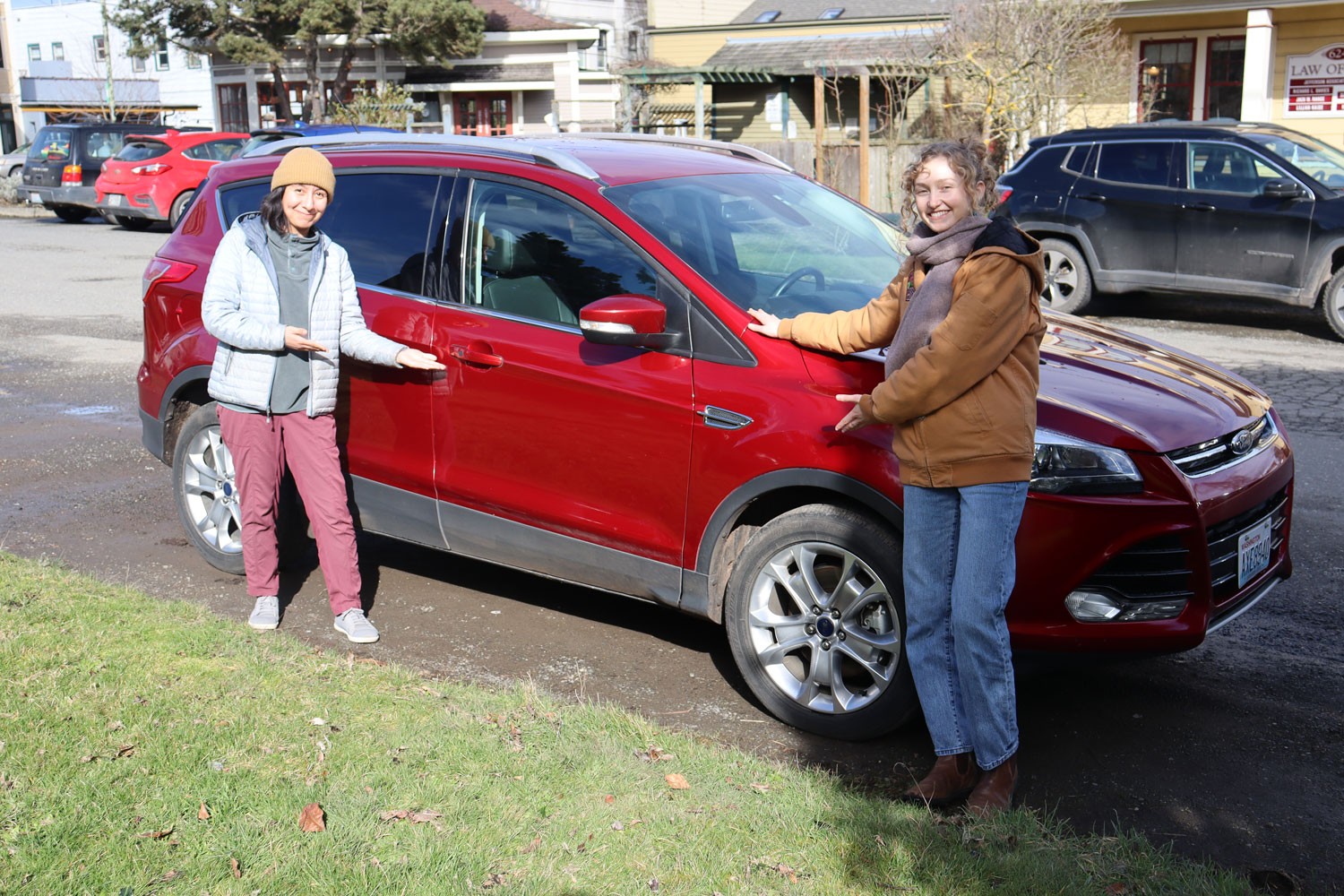Two young women pose on either side of a bright red shiny SUV.