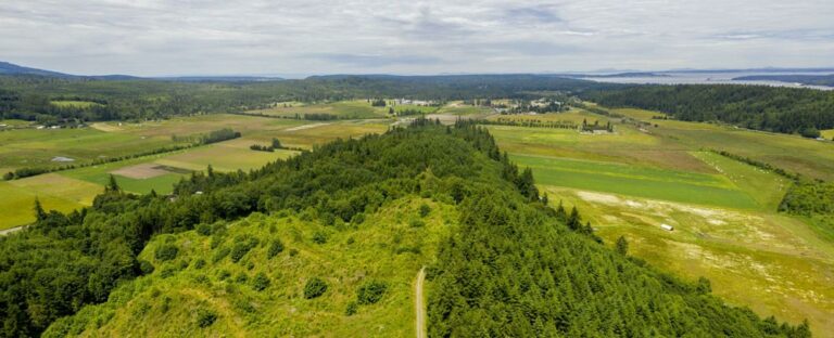 Photo of the tip of a forested ridge with farmland in the background.