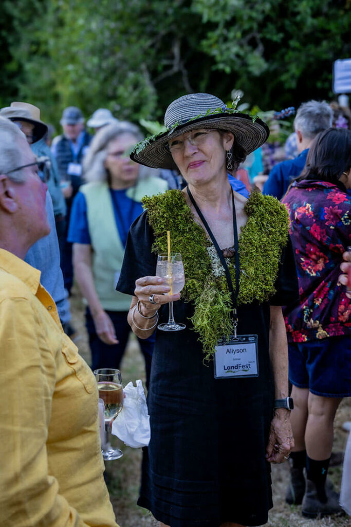 Woman in black dress, straw hat with ferns, and moss stole in crowd