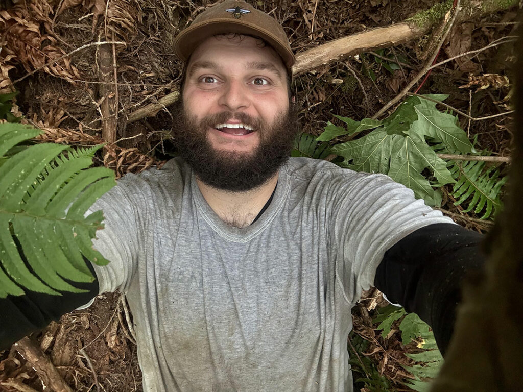 Selfie of young bearded man in baseball cap on forest floor