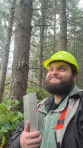 Man with a beard in a yellow hard hat holding a clipboard.
